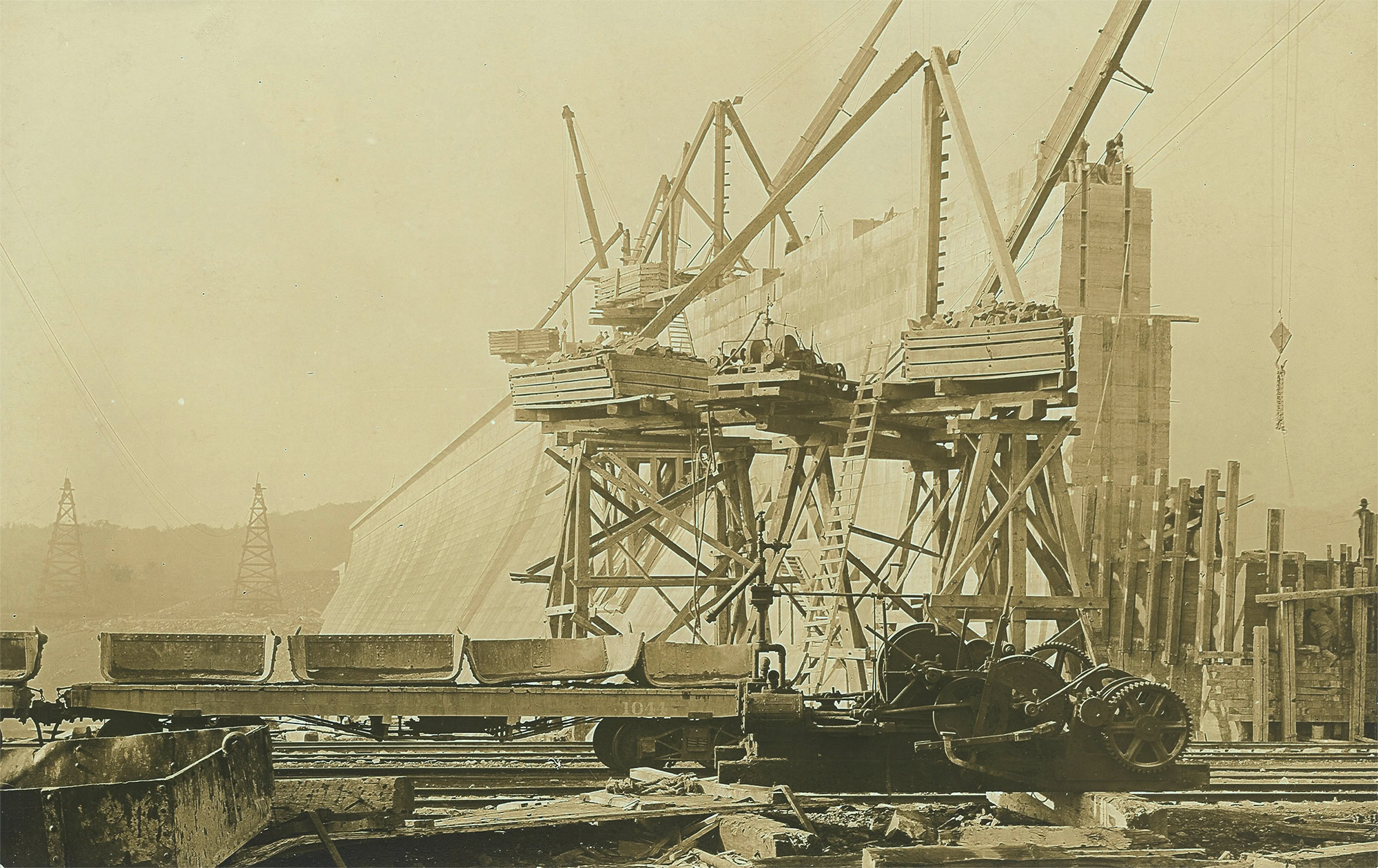 A large cement wall with scaffolding and a railway car in front.